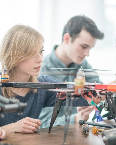 A group of students is working on building a machine with drone parts, they are learning and working together in a university class.